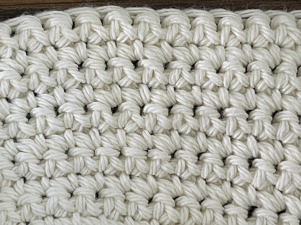 Close-up of cream-colored single-crochet fabric with visible rows and individual stitches.